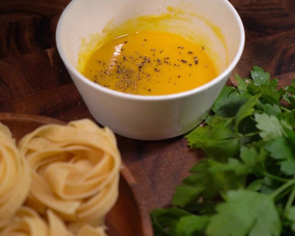 Copos de pimienta negra gruesa esparcidos sobre una salsa suave de huevo y queso en un bol blanco.