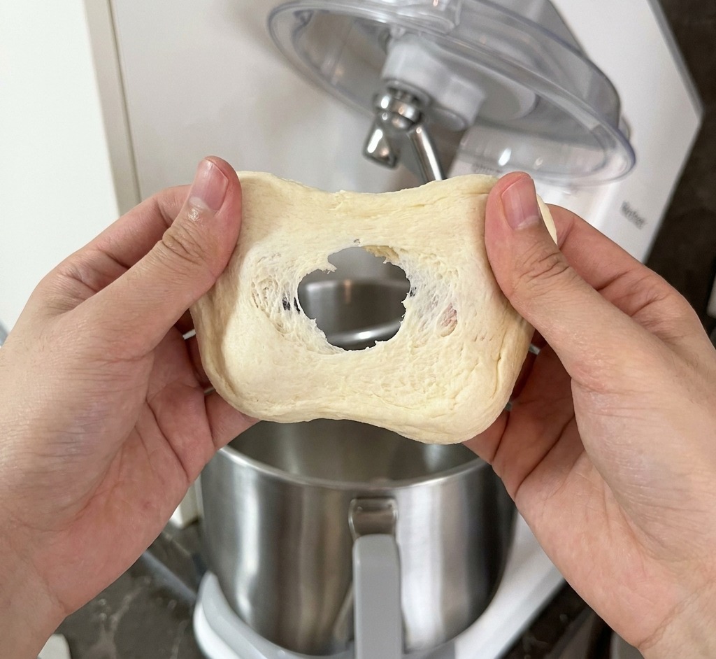 Una persona estirando un trozo de masa pálida entre las manos para comprobar la formación de la membrana de gluten.