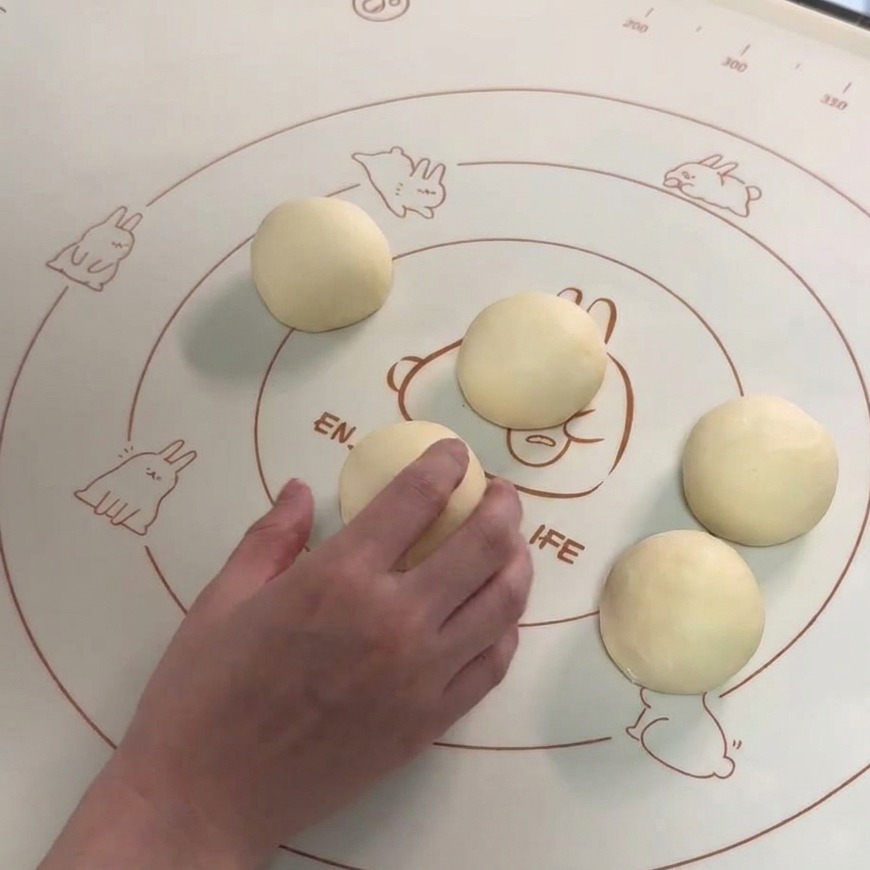 Seis bolas de masa lisas dispuestas sobre un tapete de silicona con una mano boleando una de las porciones.