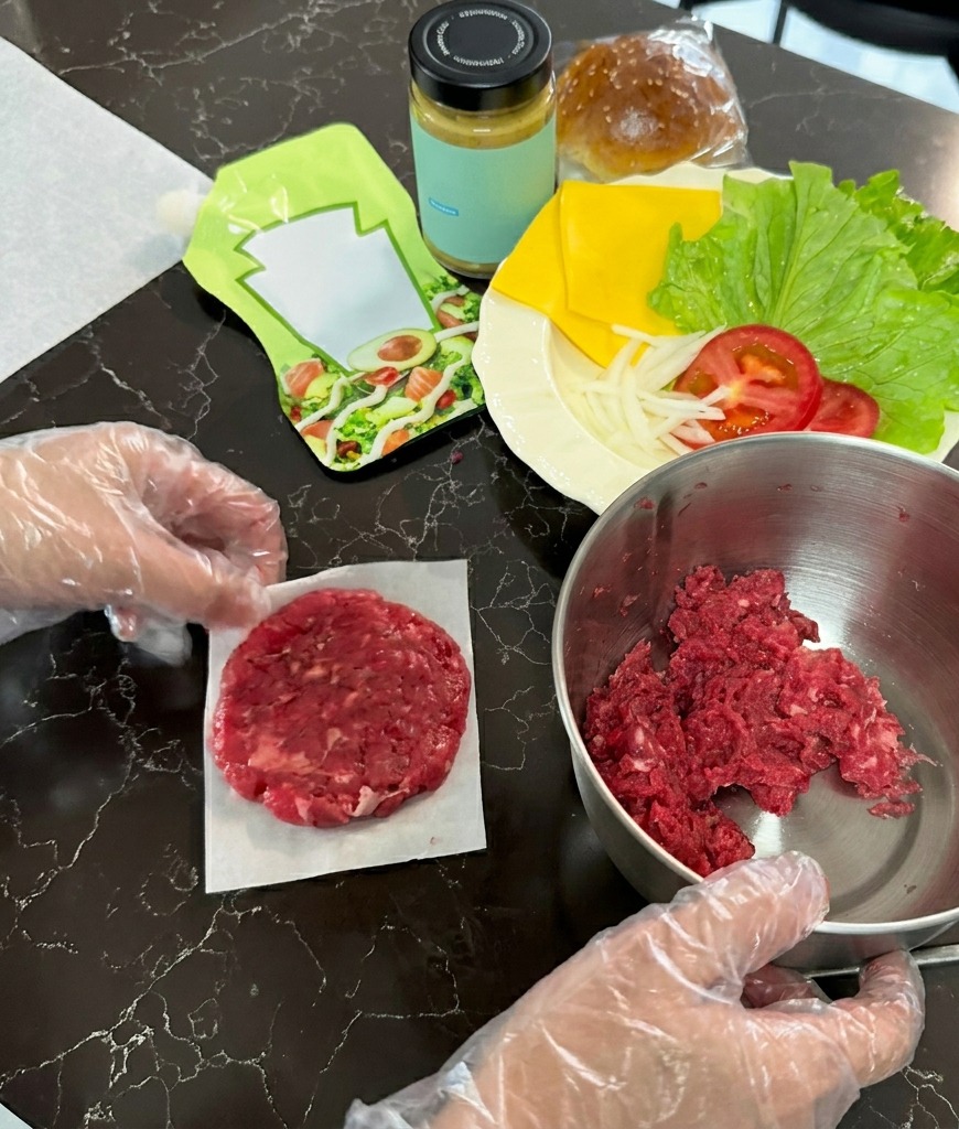 Una hamburguesa cruda aplastada en un círculo fino sobre un cuadrado de papel vegetal junto a un bol de carne.