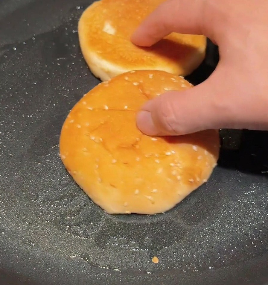 Panes de hamburguesa partidos por la mitad tostándose en una sartén seca hasta que la superficie esté dorada.