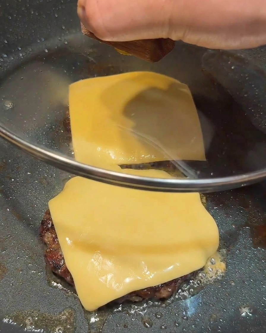 Una tapa de cristal cubriendo la sartén con dos medallones de carne cubiertos de queso.