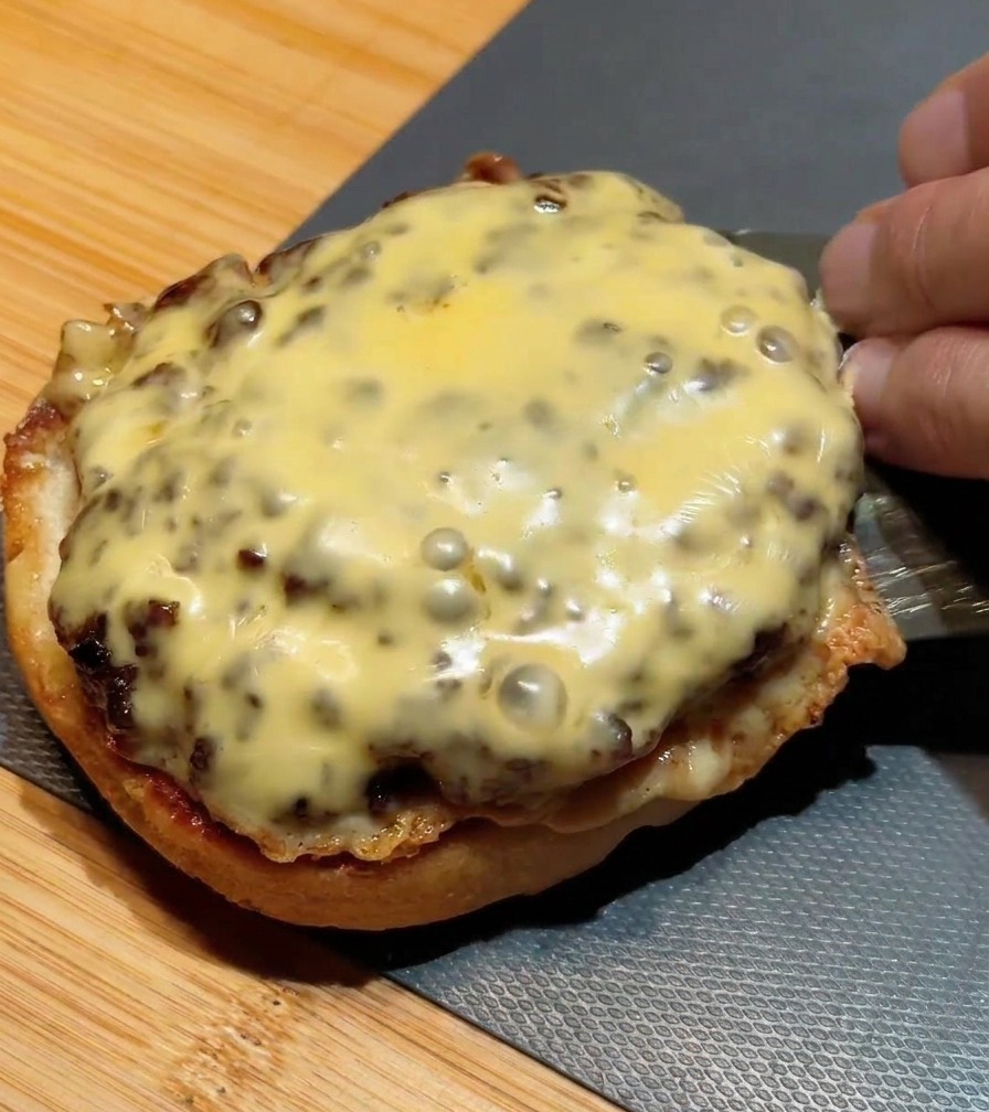 Una espátula metálica apilando un segundo medallón con queso fundido sobre el primero que ya está en el pan.
