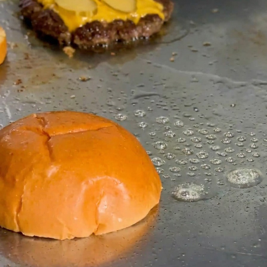 La parte superior de un pan brioche tostándose en la plancha con grasa burbujeando en los bordes.