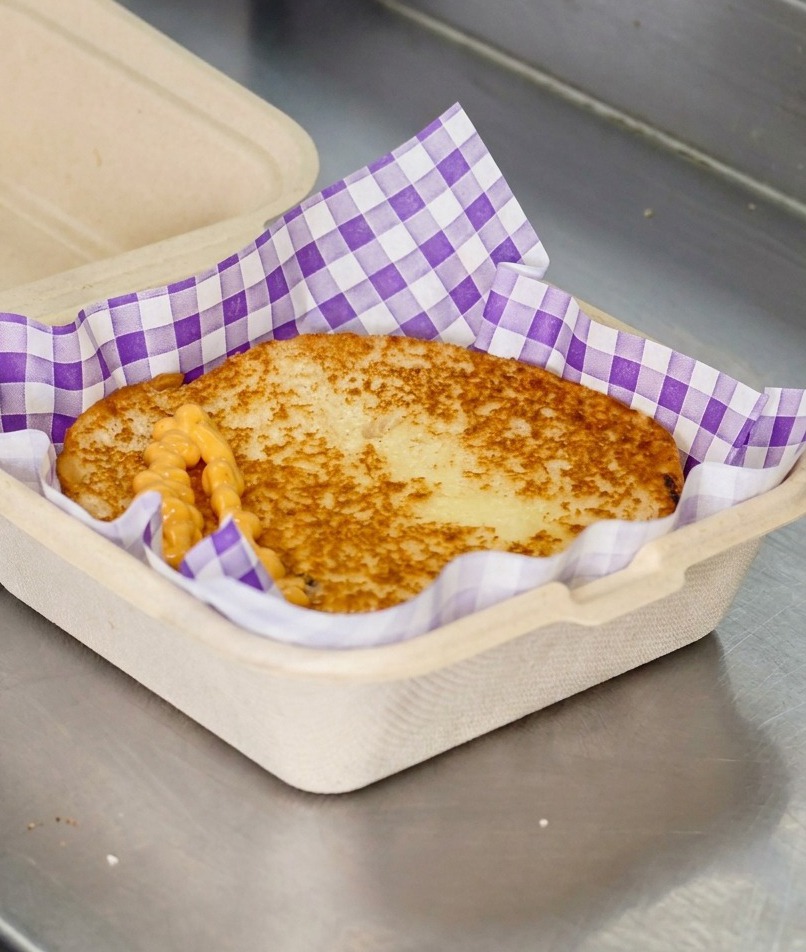 Salsa cremosa de color naranja para hamburguesa cayendo en zigzag sobre un pan tostado dorado.