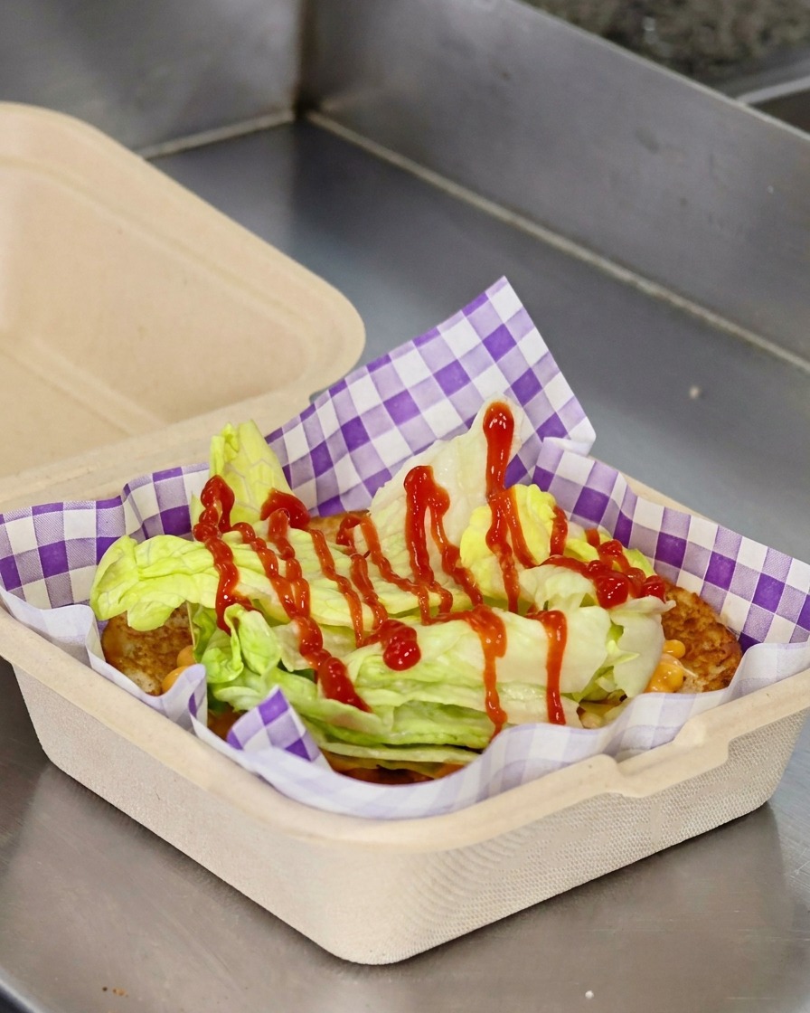 Rodajas de tomate rojo y una hamburguesa con queso apilándose sobre la lechuga dentro del pan tostado.