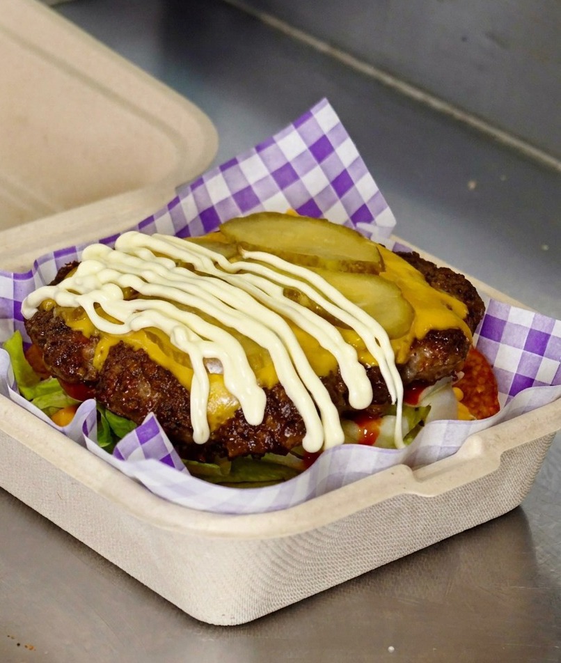 Mayonesa blanca cayendo sobre las rodajas de pepinillo en una hamburguesa con queso.