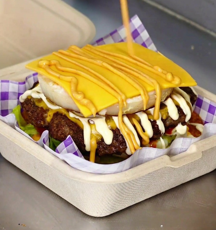 Una hamburguesa gourmet terminada con un huevo frito visible y queso fundido entre panes brioche tostados.