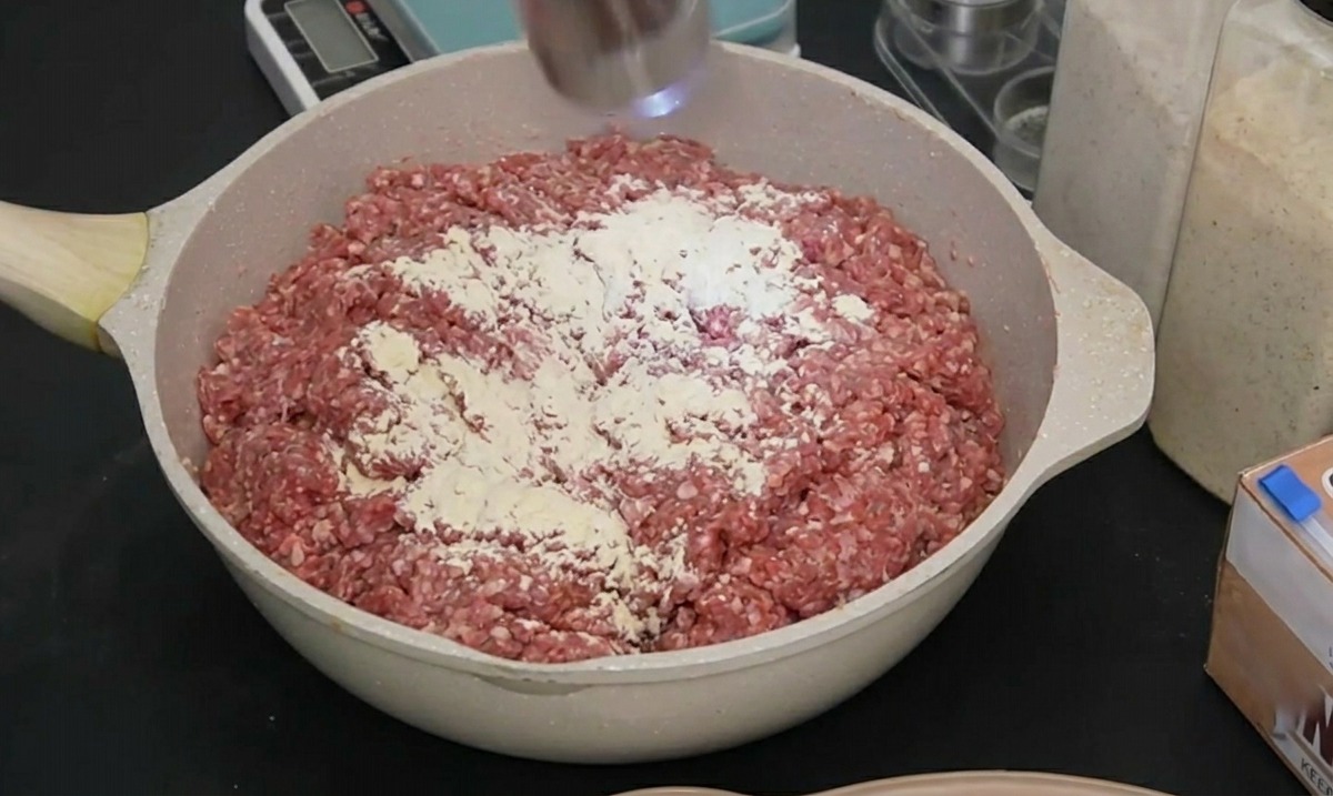 Un molinillo eléctrico de acero inoxidable moliendo pimienta negra sobre la carne cruda sazonada.