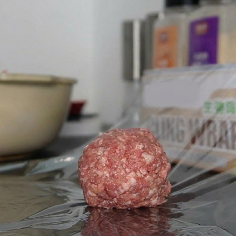 Una porción redonda de carne molida sazonada sobre un trozo de papel film transparente en la encimera.