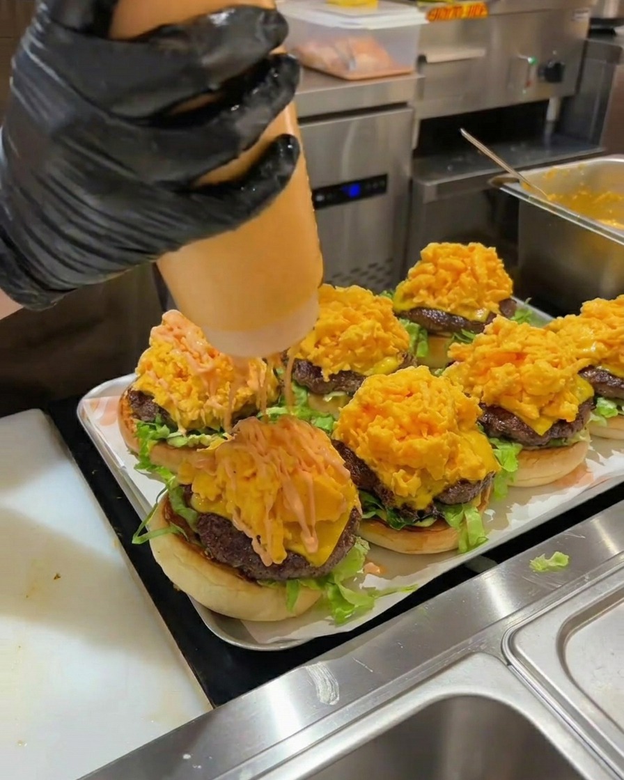 Salsa de hamburguesa naranja vertiéndose sobre una pila de huevos revueltos en una hamburguesa montada.