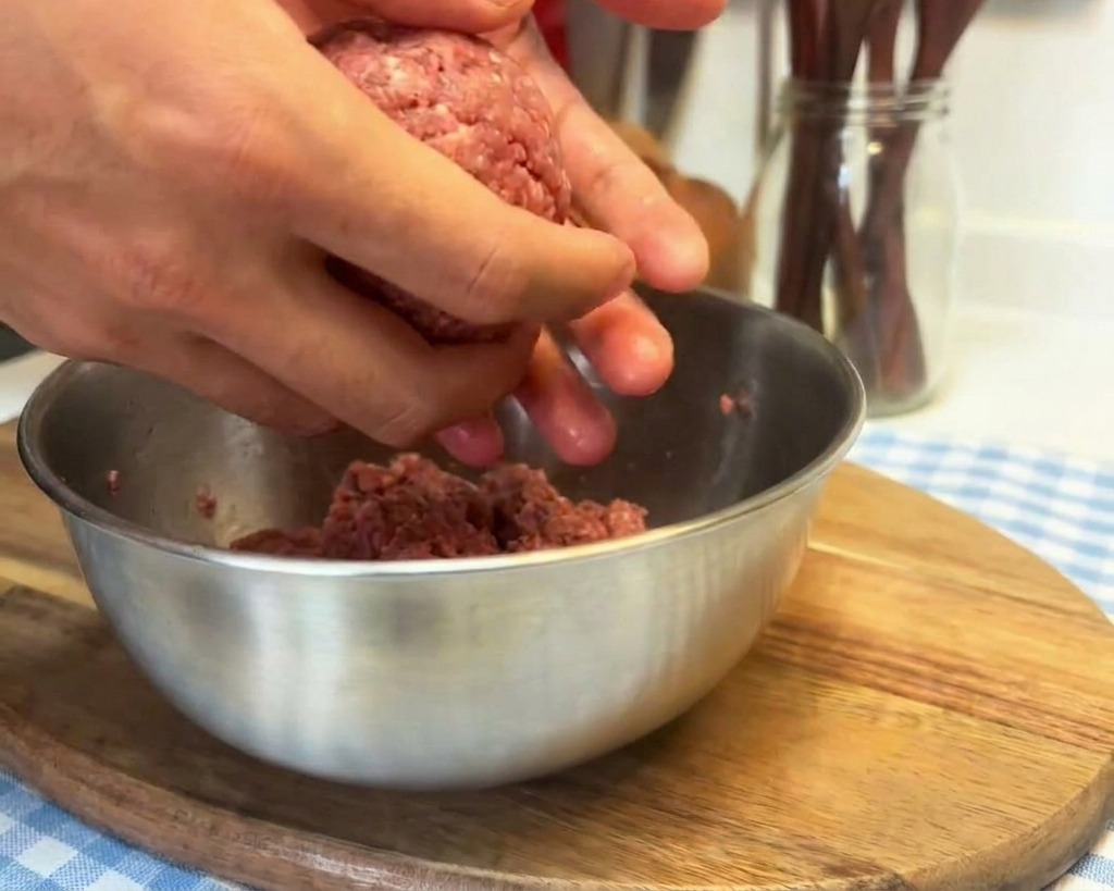 Manos trabajando una bola de carne picada golpeándola contra la palma para compactarla.