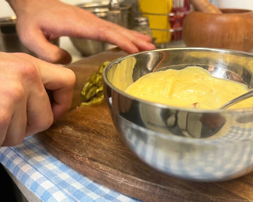 Pepinillos verdes picados cayendo en un bol con mayonesa, mostaza y kétchup para hacer la salsa.