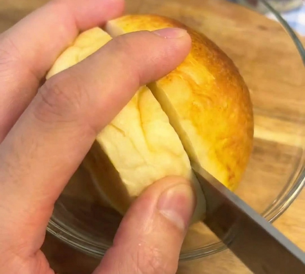 Cuchillo de sierra cortando por la mitad un pan brioche dorado y perfectamente tostado.