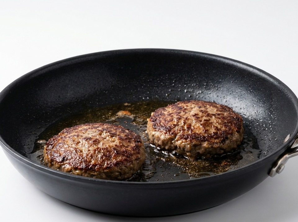 Dos hamburguesas selladas dadas la vuelta en la sartén, mostrando una costra marrón muy oscura.