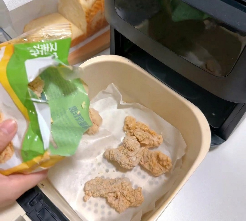 Trozos de pollo empanado congelados cayendo en una cesta de freidora de aire forrada con papel pergamino.