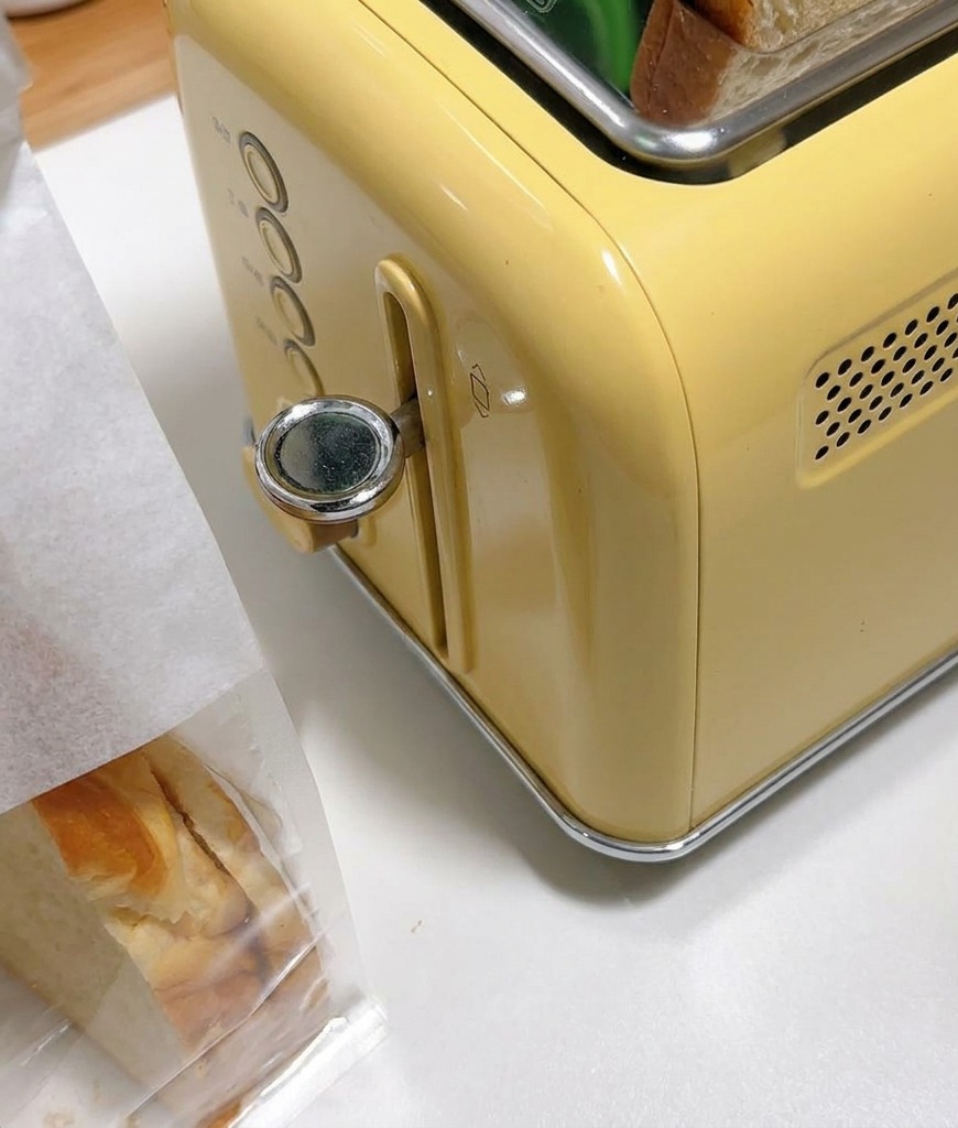 Rebanadas gruesas de pan blanco en las ranuras de una tostadora amarilla de estilo vintage.