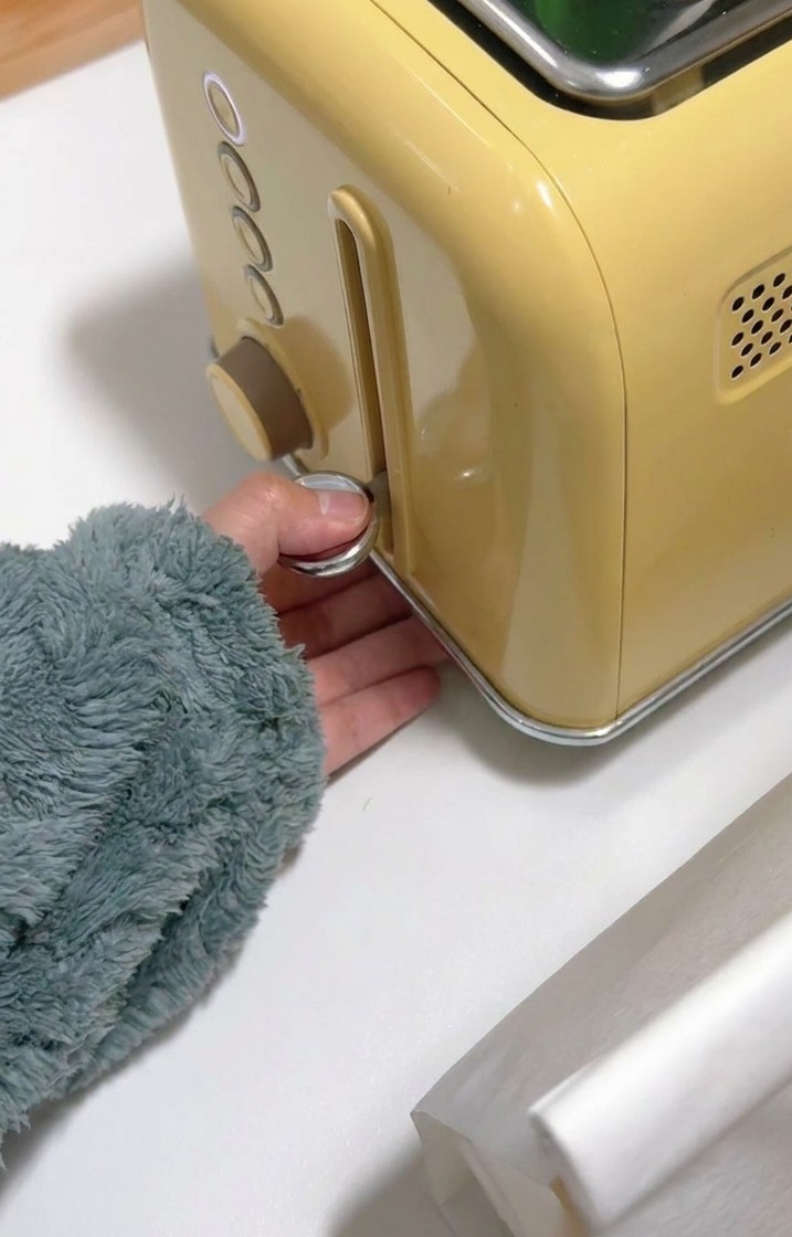 Una mano bajando la palanca cromada de una tostadora amarilla.