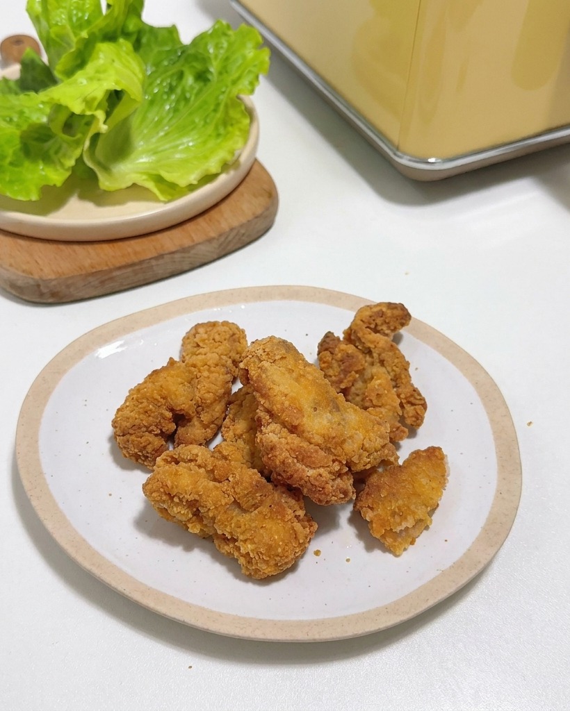 Pollo frito crujiente apilado en un plato blanco junto a hojas de lechuga fresca.