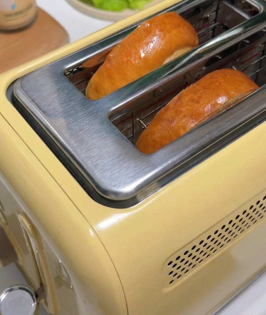 Dos rebanadas de pan tostado saliendo de una tostadora amarilla.