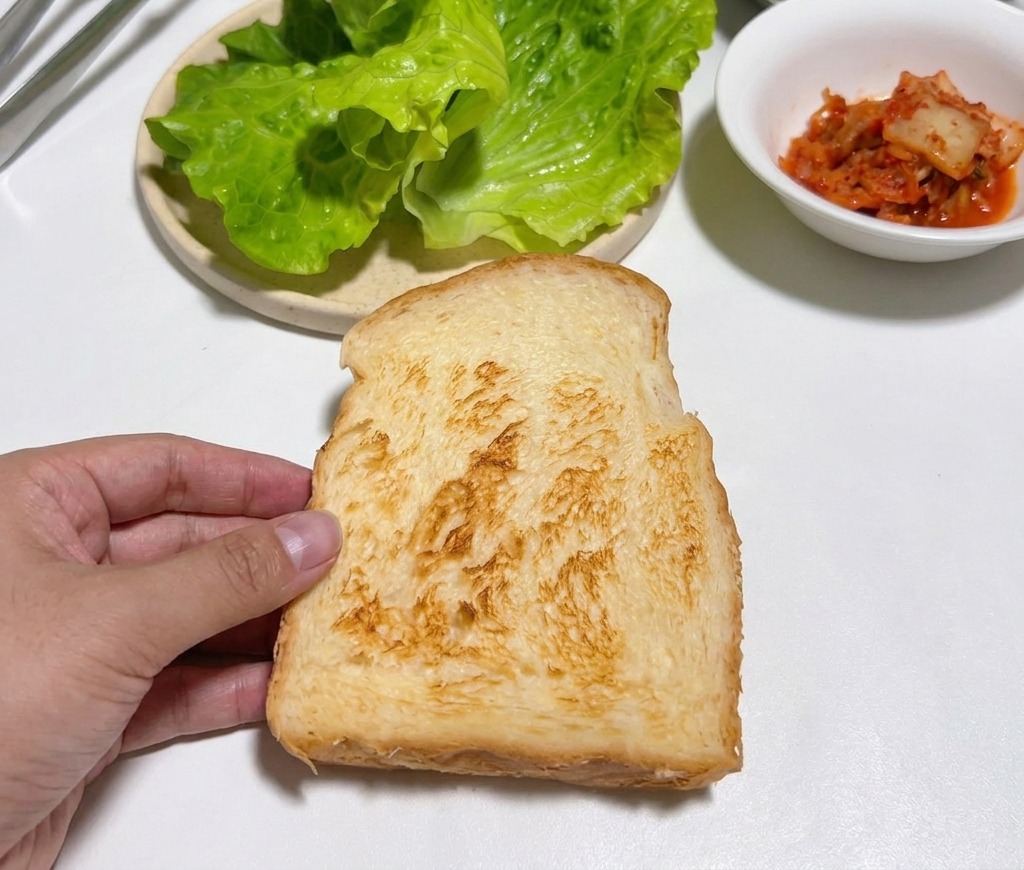 Una mano sosteniendo una rebanada de pan tostado sobre una mesa blanca.