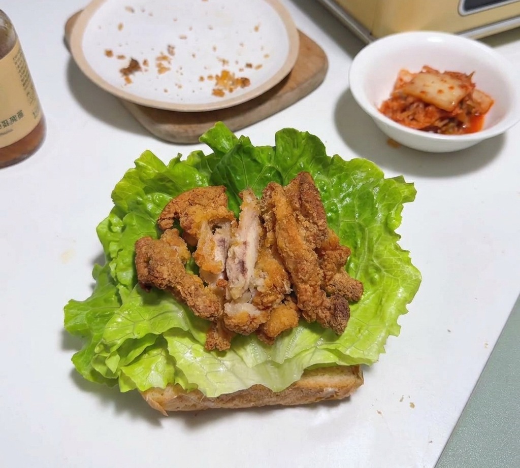 Trozos de pollo frito sobre una hoja de lechuga y pan tostado.