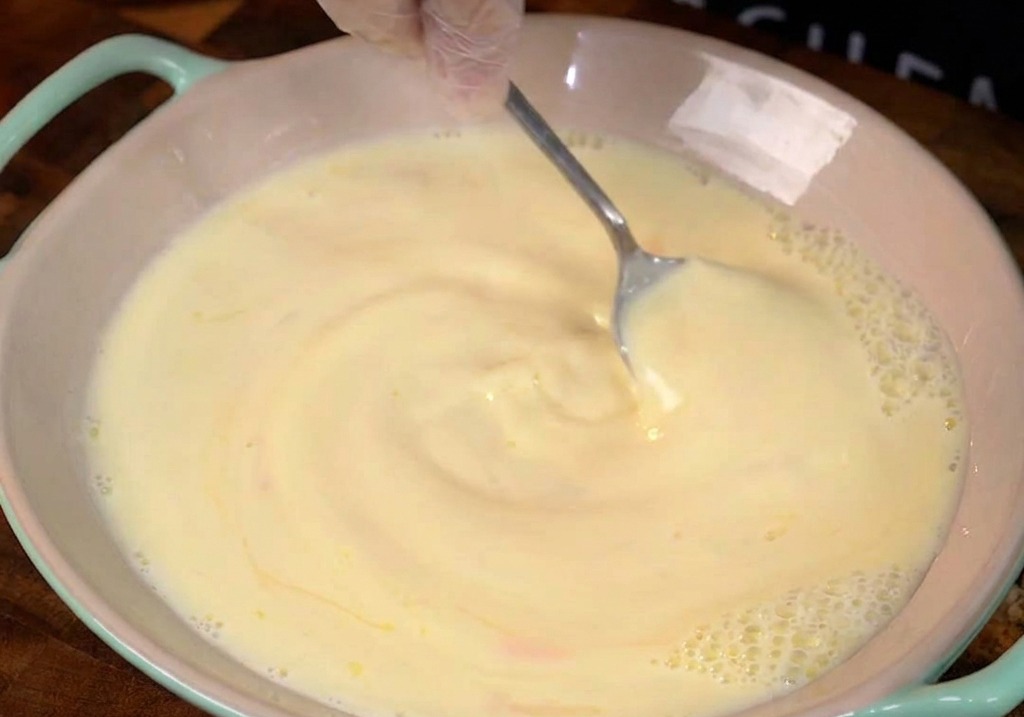 Mezcla de leche, huevos y miel en un bol de cerámica rosa.