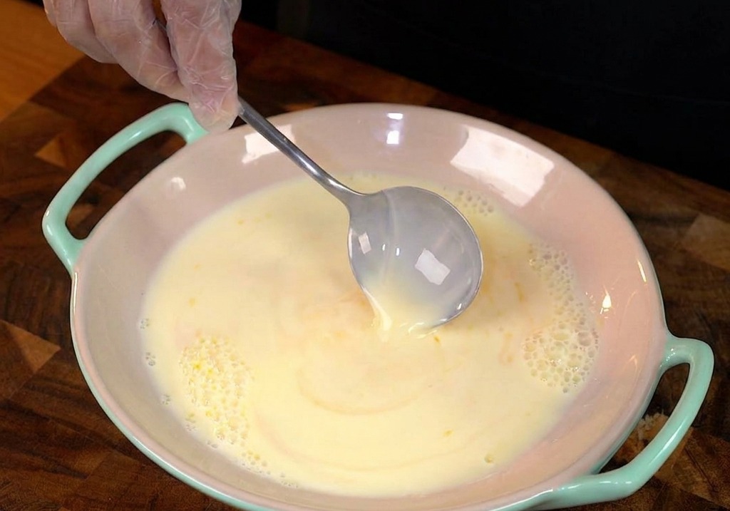 Una rebanada gruesa de pan blanco sumergiéndose en la mezcla de huevo y leche.