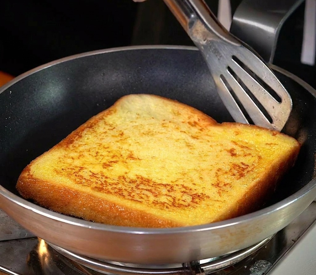 Una rebanada de pan friéndose en mantequilla derretida hasta quedar dorada.