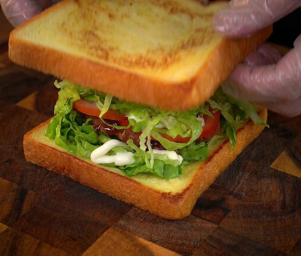 Manos colocando la última rebanada de pan tostado sobre el sándwich de pollo.