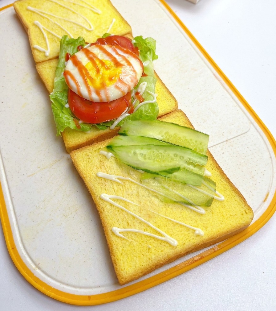 Finas rodajas de pepino fresco dispuestas diagonalmente sobre una rebanada de pan amarillo, situada junto a la primera capa del sándwich.