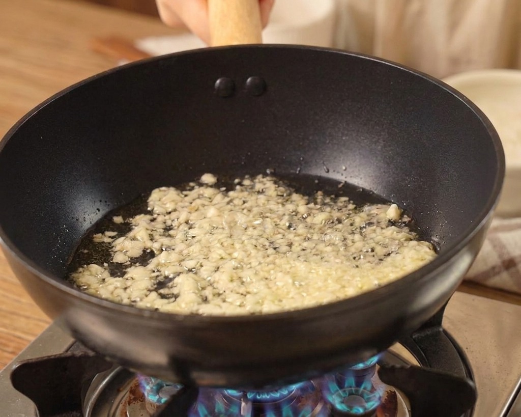 Ajo picado chisporroteando en aceite en el fondo de un wok negro sobre una llama de gas azul.