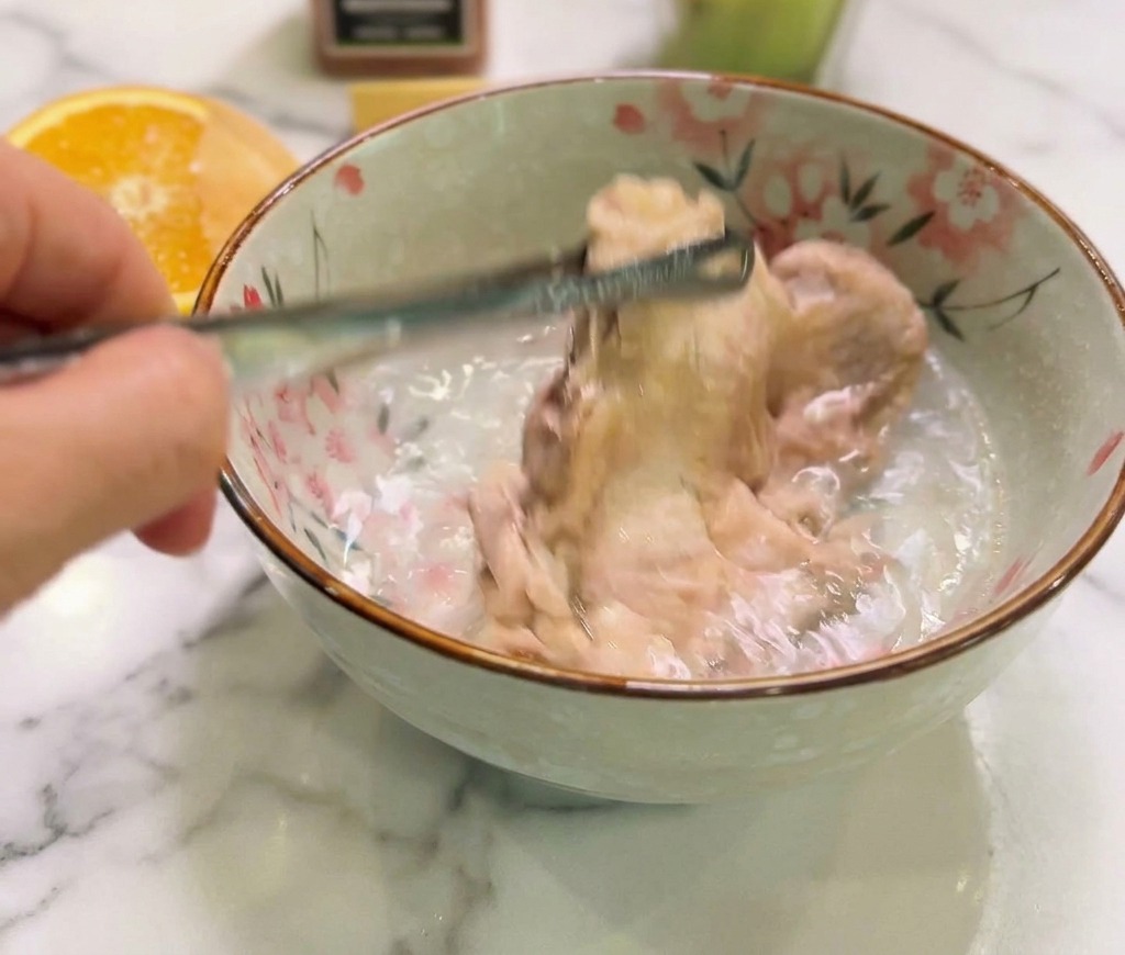 Pollo cocido siendo sumergido en un tazón de cerámica con agua fría para detener la cocción.
