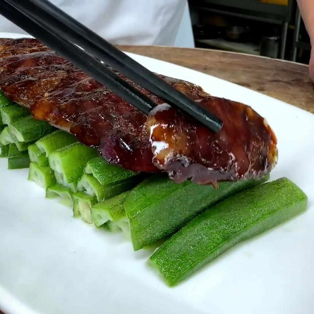 Primer plano de rodajas de salchicha china sobre una cama de okra verde en un plato blanco.