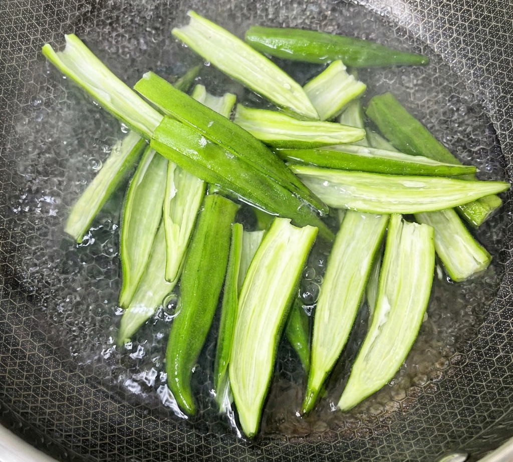 Vainas de okra abiertas hirviendo en una olla con agua en la estufa.