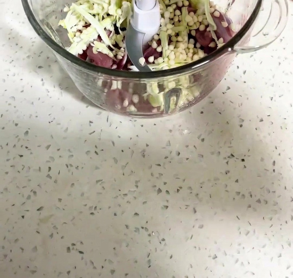 Carne de pato y semillas de okra siendo trituradas dentro del procesador de alimentos.