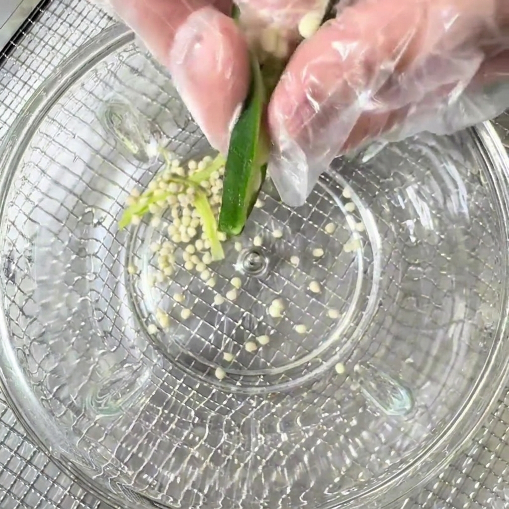 Semillas de okra siendo retiradas de las vainas cortadas hacia un cuenco de cristal transparente.