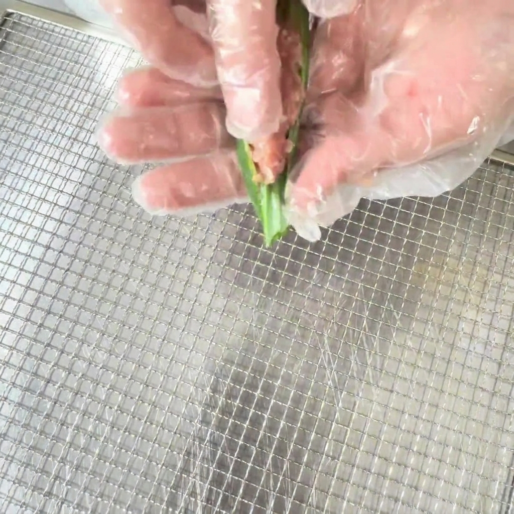 Una mano con un guante de cocina rellenando la mezcla de pato en una vaina de okra cortada por la mitad.