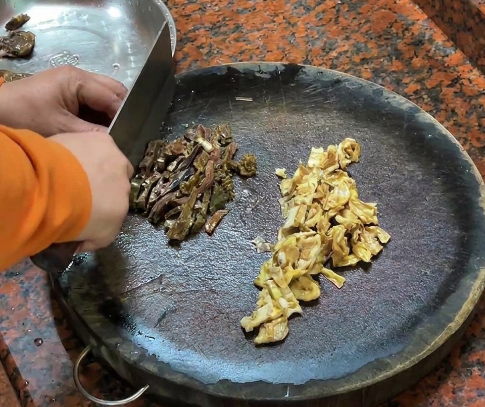Salchicha de hígado de pato picada y trozos de piel de pato sobre una tabla de cortar de madera.