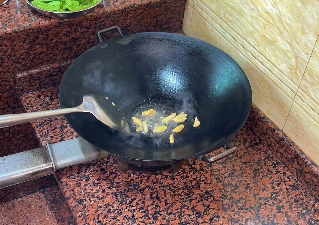 Trozos de piel de pato friéndose en un wok caliente y seco, soltando grasa líquida.
