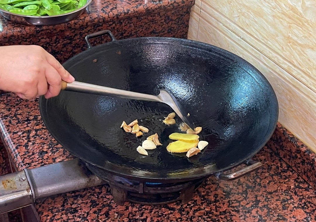 Rodajas de jengibre y ajo salteándose en la grasa de pato fundida dentro de un wok.
