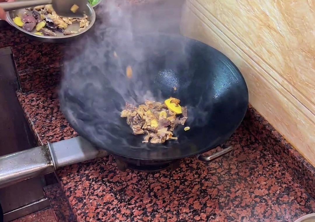 Trozos de salchicha de hígado de pato salteándose con aromáticos en el wok.