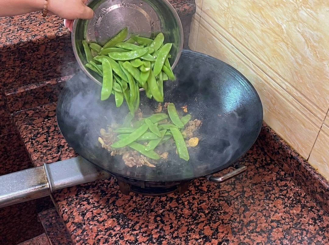 Tirabeques frescos siendo añadidos al wok con la salchicha y los aromáticos.