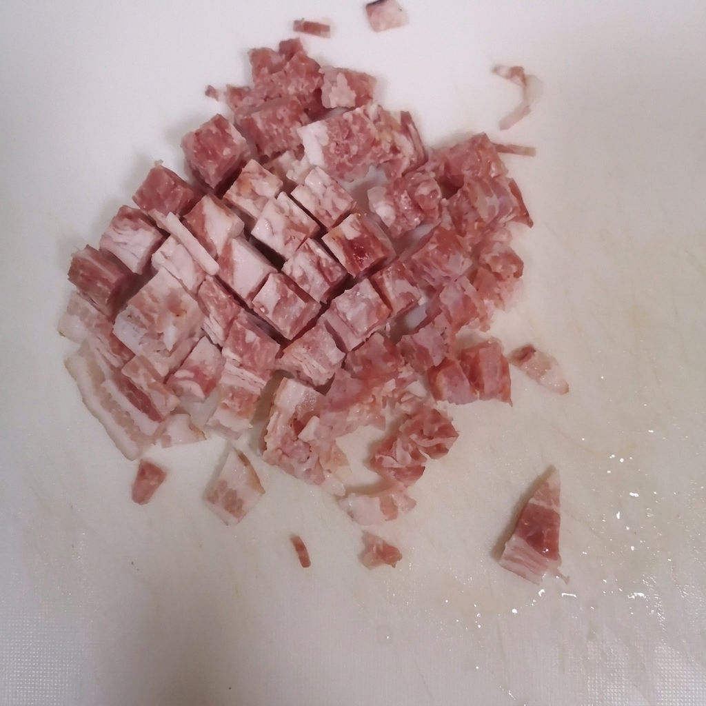 Lonchas de bacon cortándose en cubitos sobre una tabla de cortar limpia.