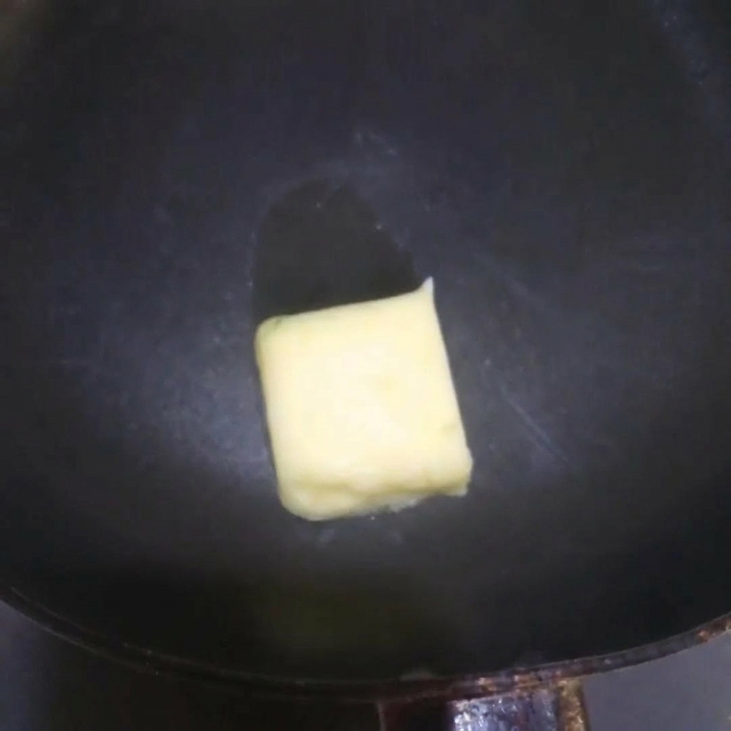 Mantequilla amarilla derritiéndose y chisporroteando en una sartén caliente.