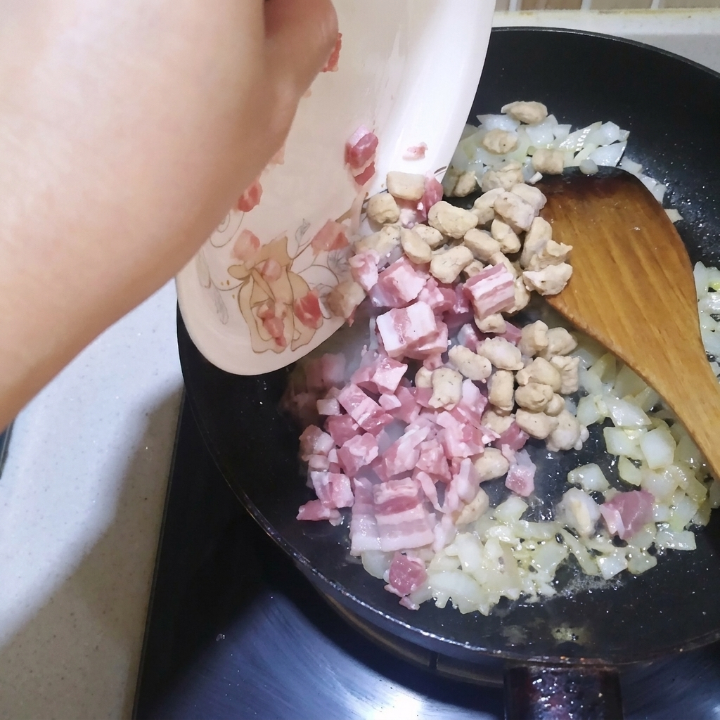 Cubitos de bacon y ternera sofríendose en una sartén con cebolla y ajo.