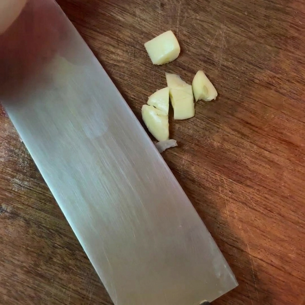 Dientes de ajo troceados junto a un cuchillo grande sobre una superficie de madera.