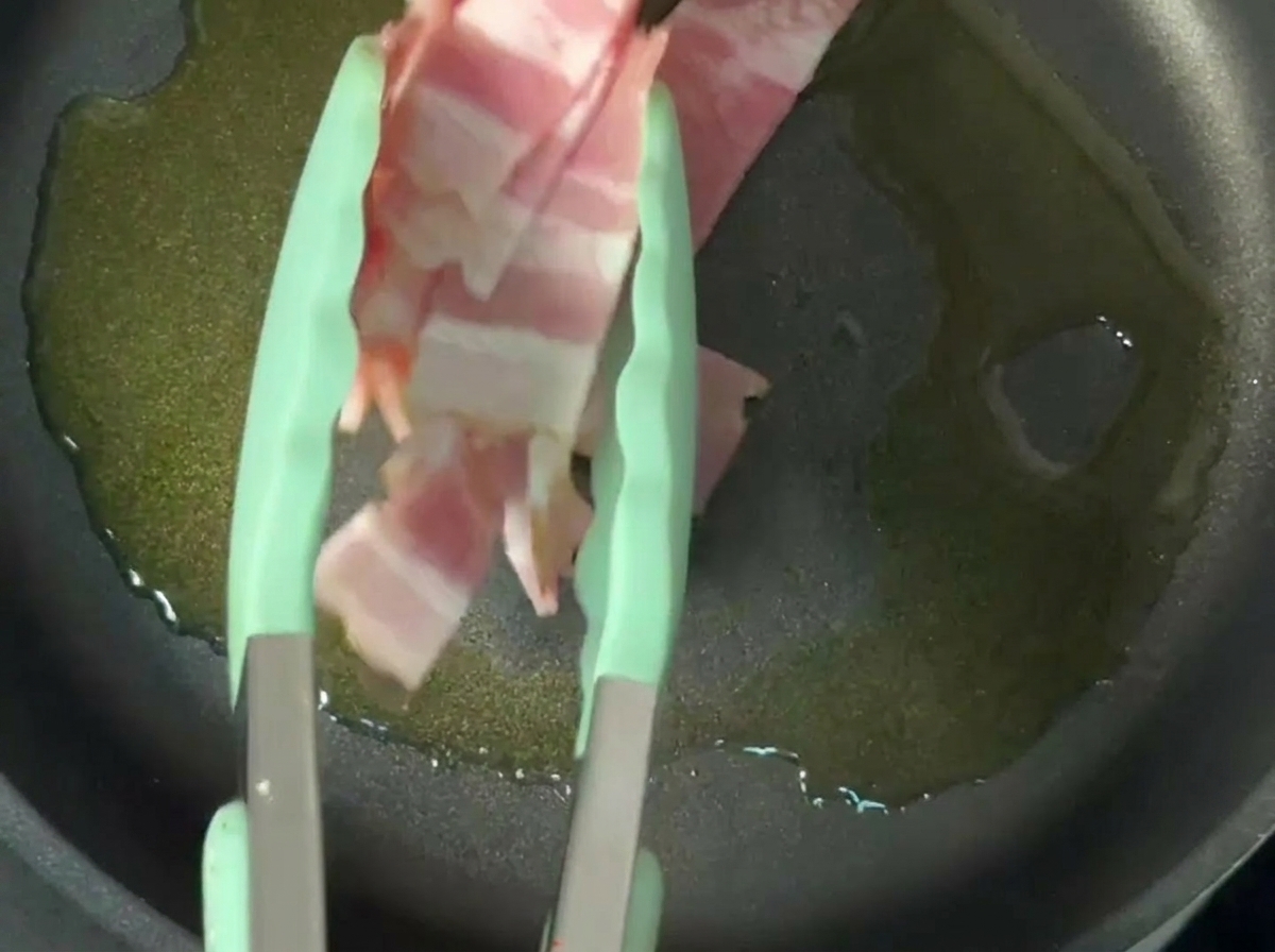 Tiras de bacon friéndose en aceite de oliva en una sartén antiadherente.