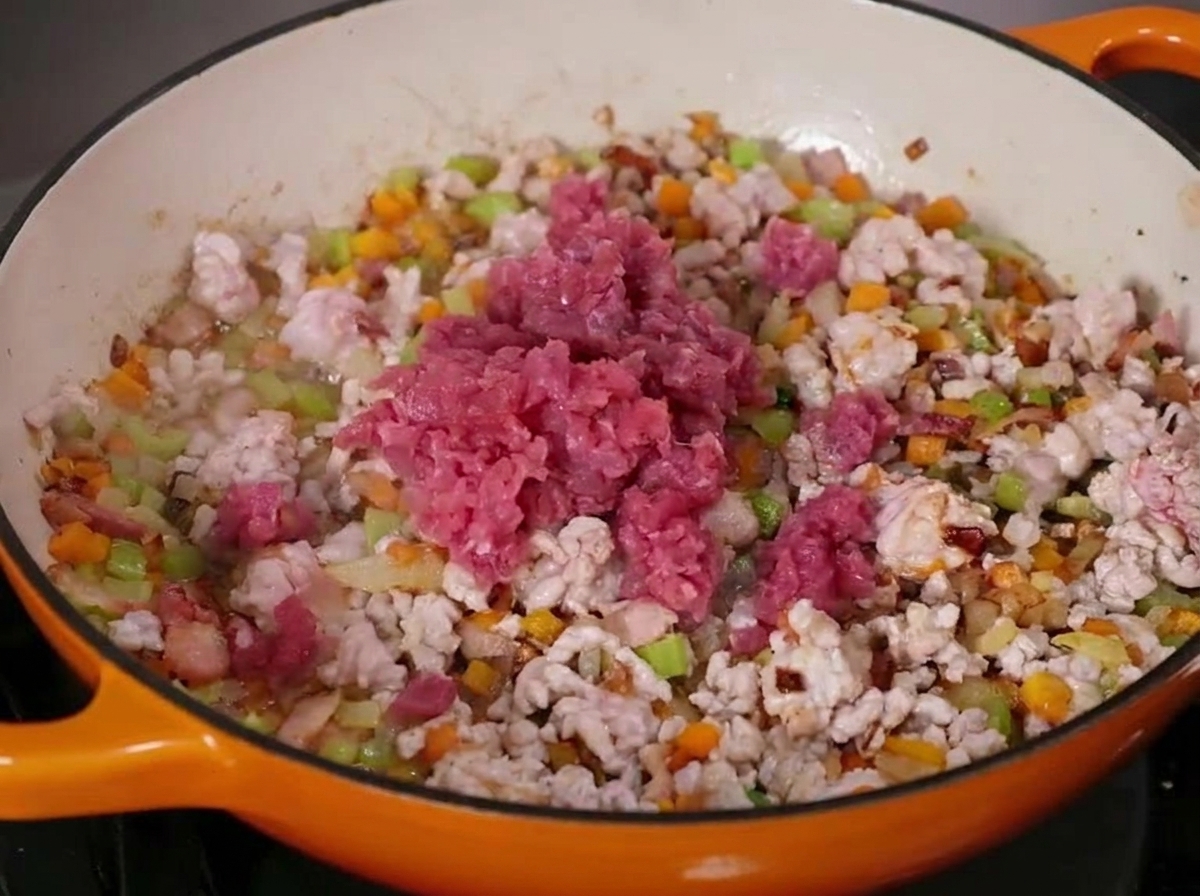 Carne de ternera y cerdo cocinándose con verduras picadas en una gran sartén de hierro fundido esmaltado.