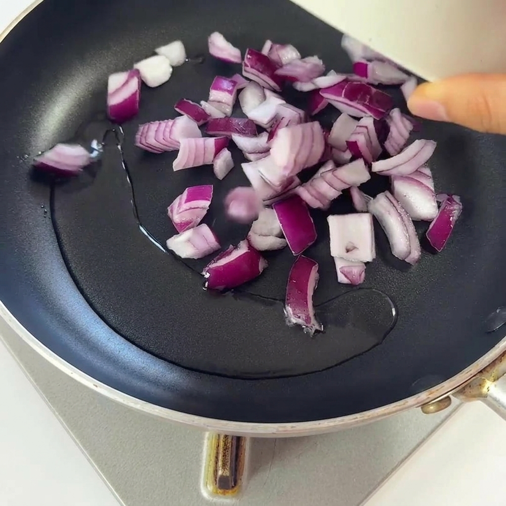 Cebollas picadas friéndose en una sartén con aceite caliente brillante.